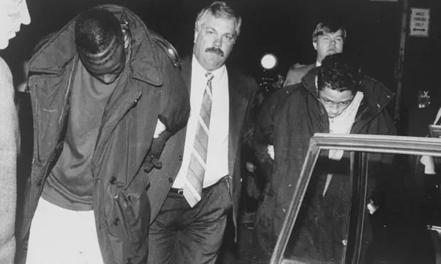 Yusef Salaam, left, is led away by a detective after being arrested in Central Park.